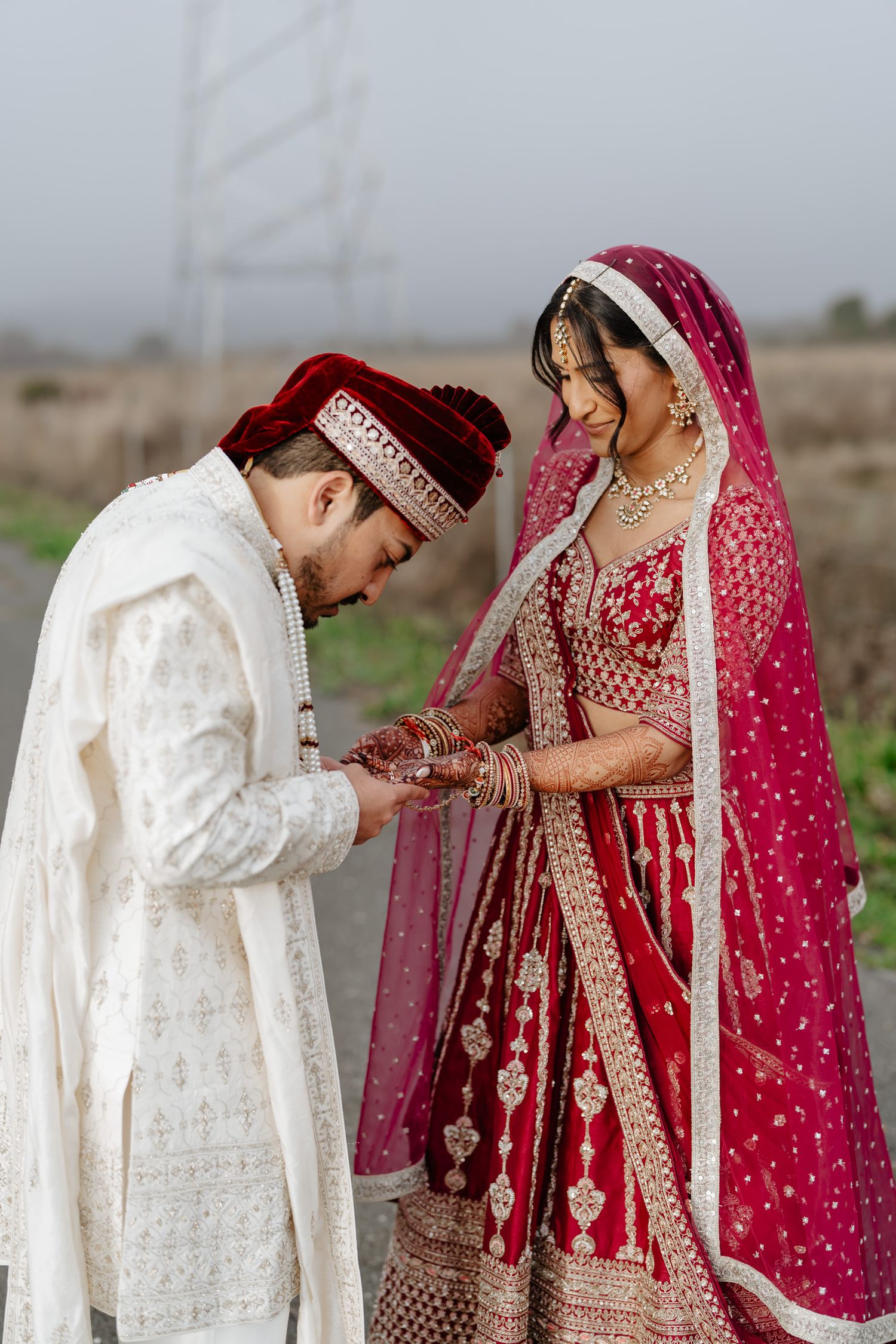 A couple in traditional South Asian wedding attire share intimate moments during an outdoor photoshoot.