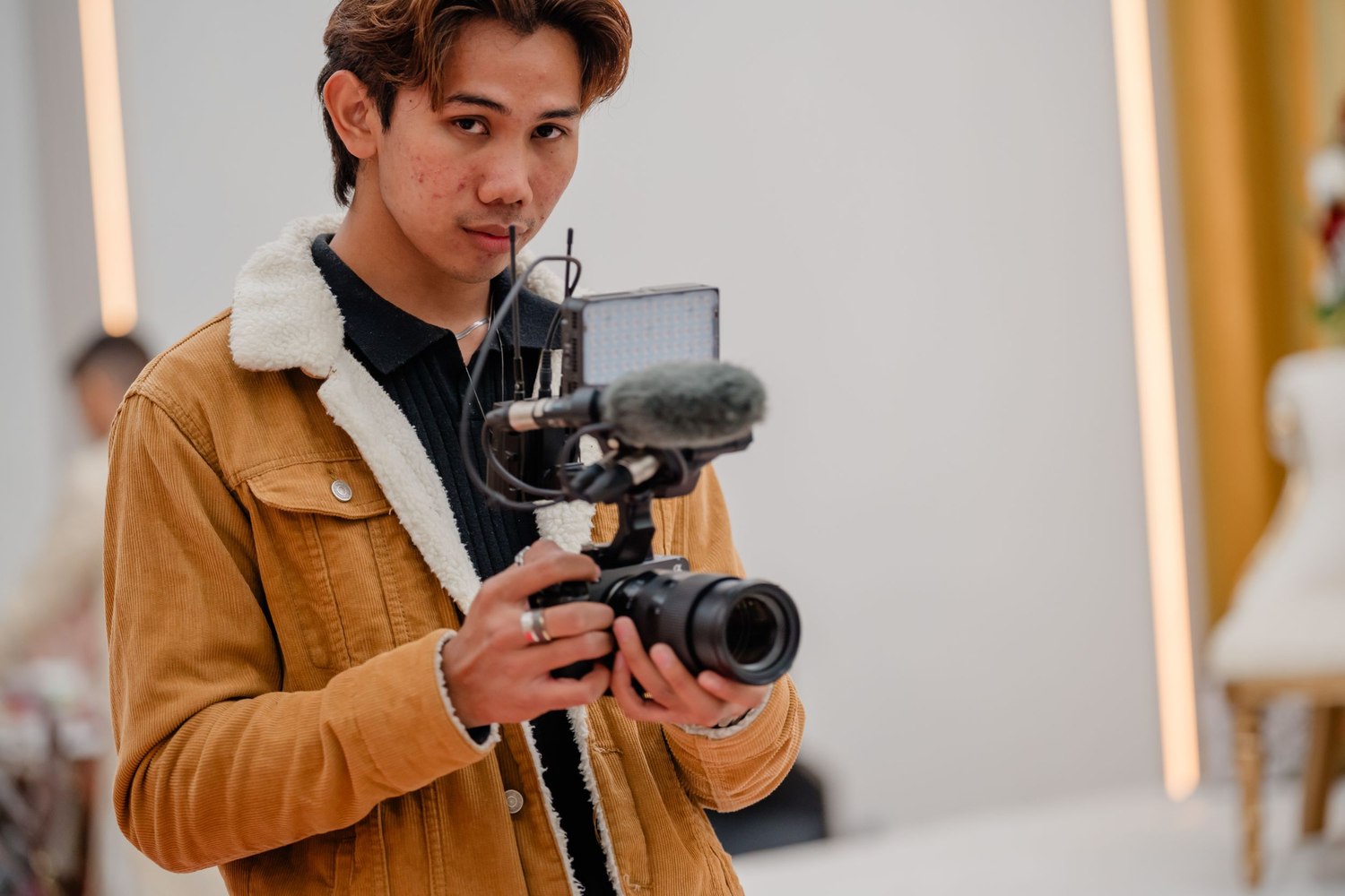 Young man in brown sherpa jacket operating a professional camera gimbal stabilizer while filming indoors.