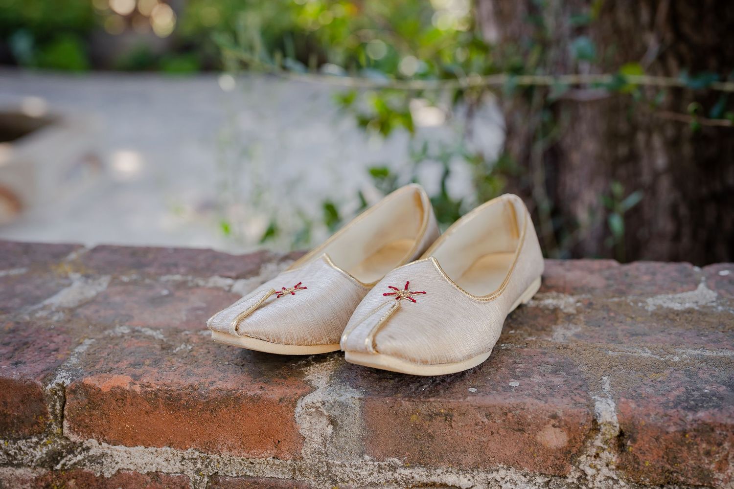 Beige leather moccasins with decorative stitching sit on a rustic brick ledge in an outdoor garden setting.