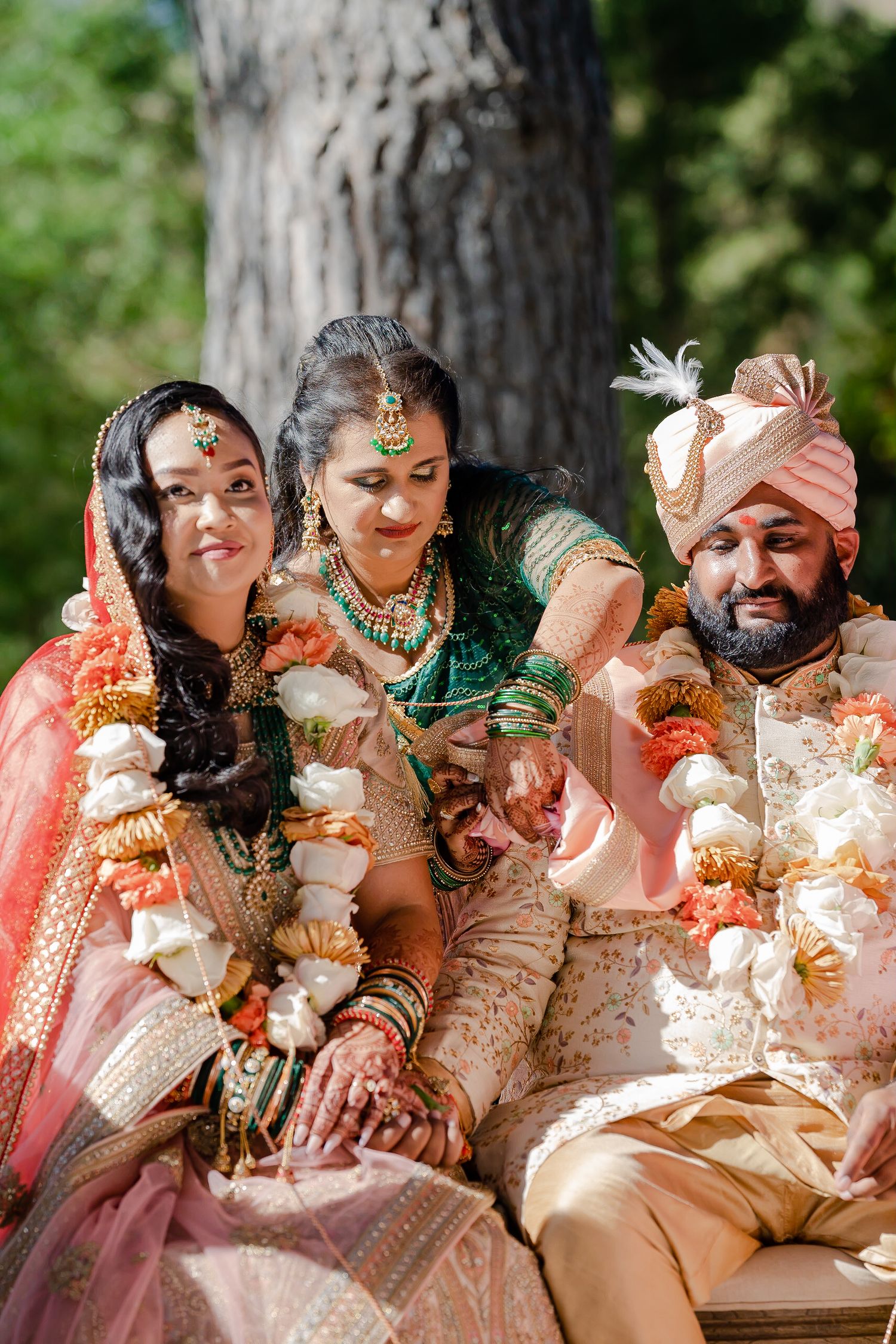 Wedding guests in traditional Indian attire with henna and jewelry sit together outdoors during a celebration.