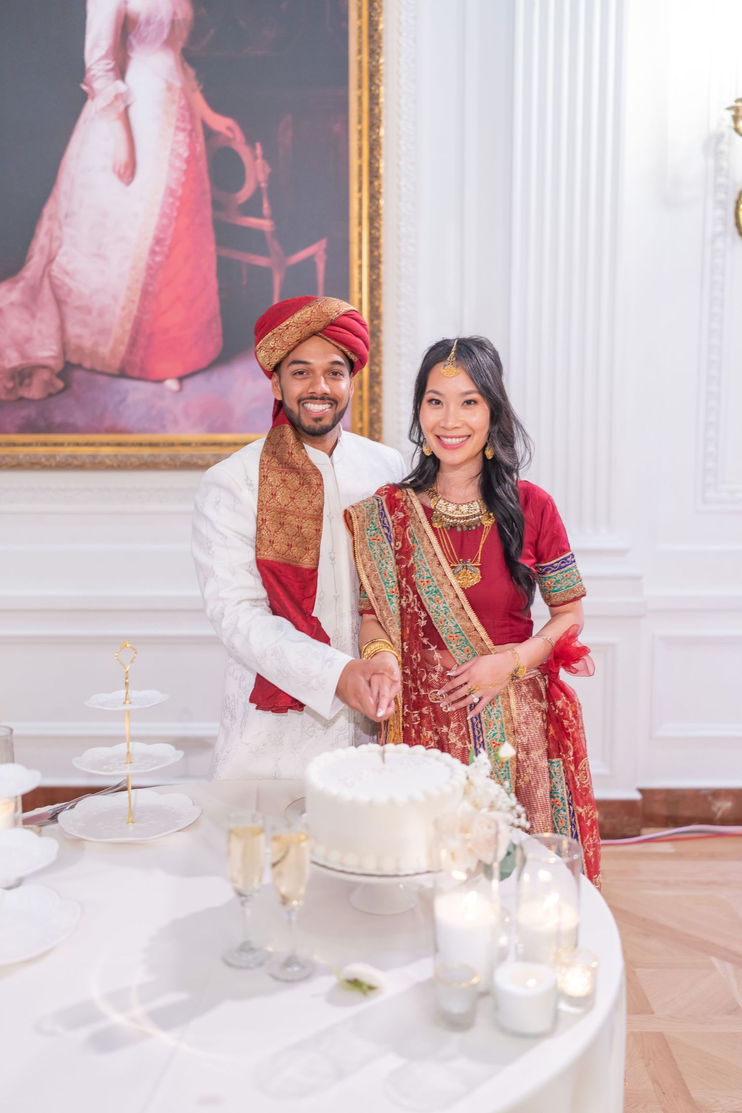 Couple in traditional Indian wedding attire seated at an elegant white table with candles.