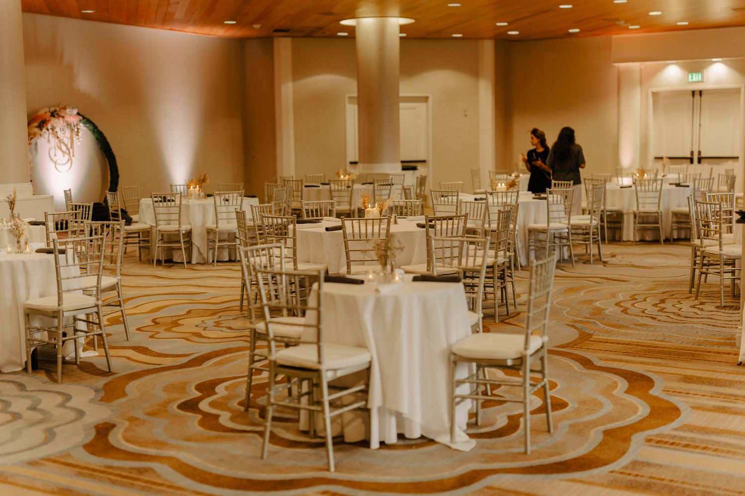 Elegant wedding reception ballroom with gold chiavari chairs, round tables with white linens, and warm ambient lighting.