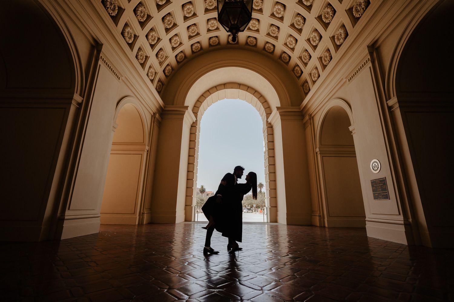 Romantic couple silhouette dancing under ornate arched corridor with decorative ceiling in elegant venue.