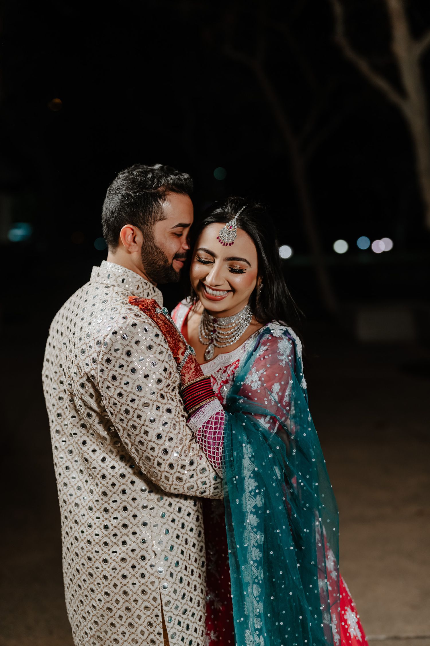 A couple shares an intimate moment in traditional Indian wedding attire with the groom in white and bride in turquoise.
