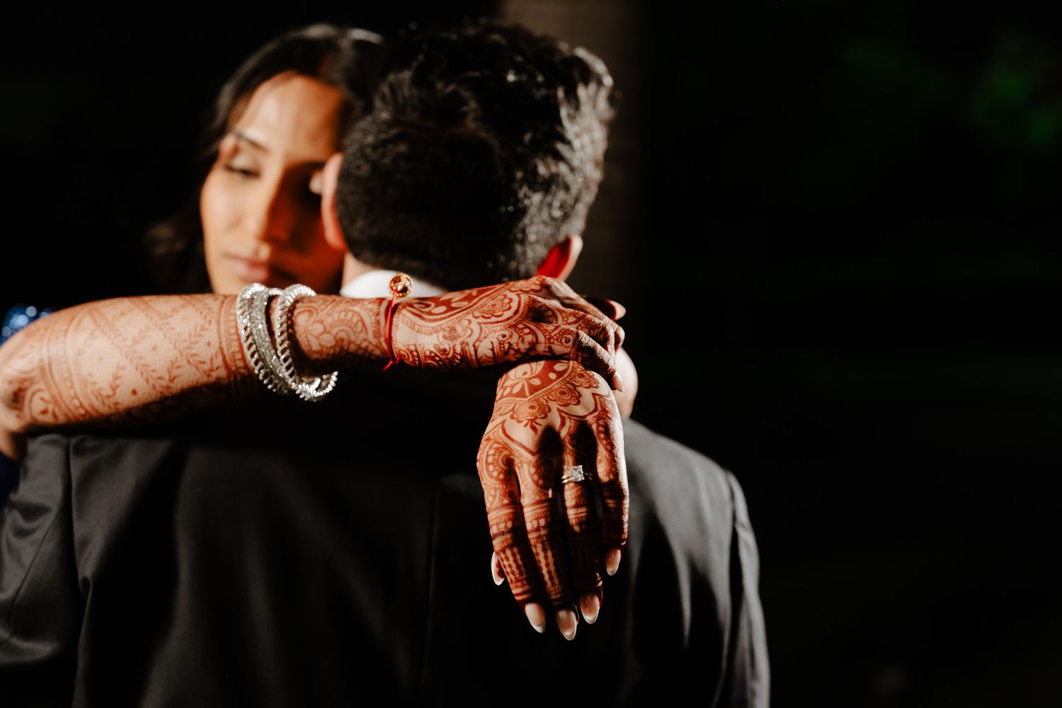 Close-up view of hands wearing traditional Indian wedding jewelry and henna designs during a cultural ceremony.