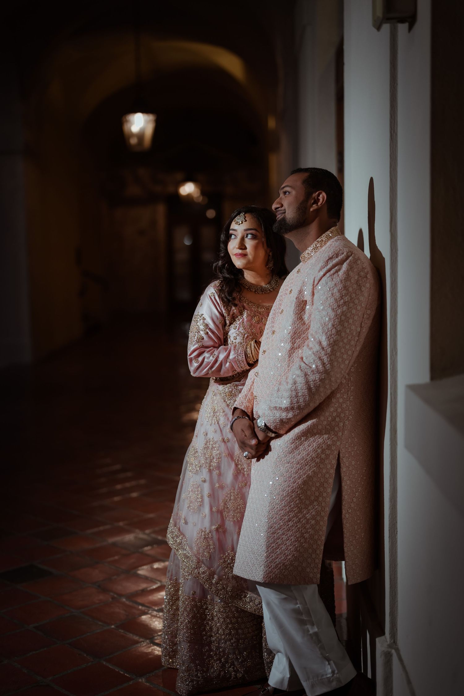 A couple in matching pink and white outfits share an intimate moment against a dimly lit hallway wall.
