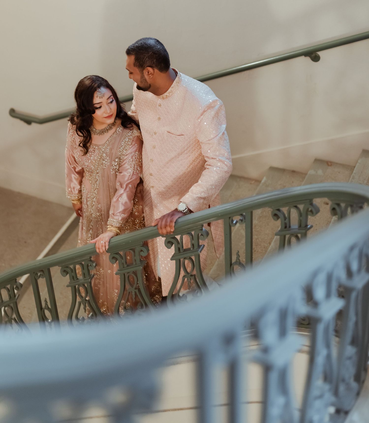 A romantic couple shares an intimate moment on an ornate staircase with decorative railings.