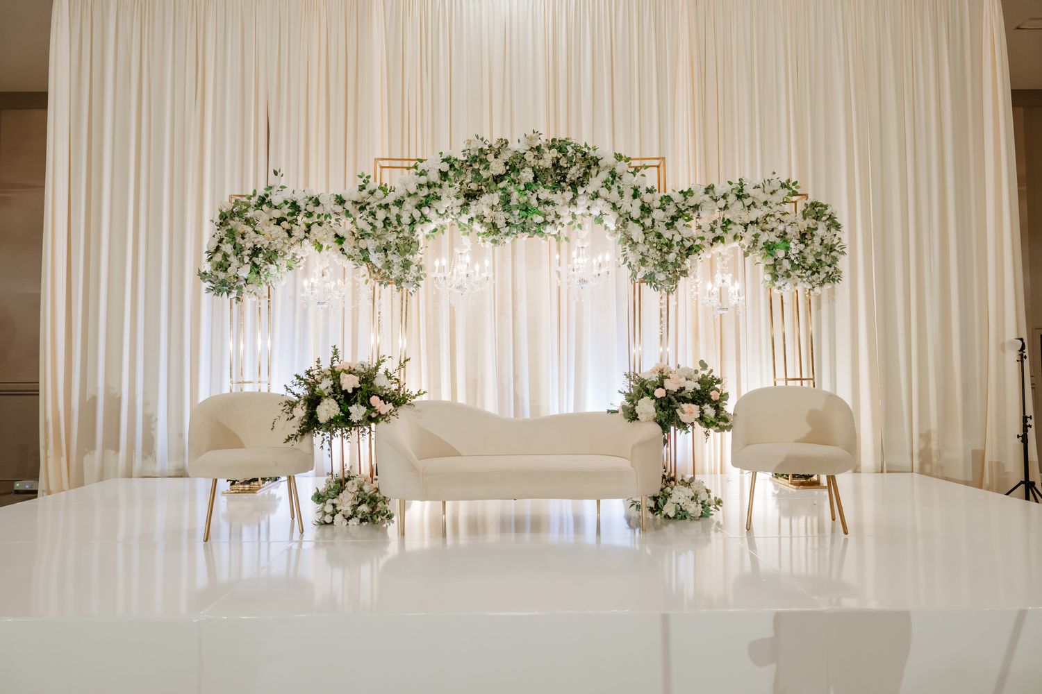 Elegant white wedding reception hall decorated with draped fabric and floral arrangements along the walls.