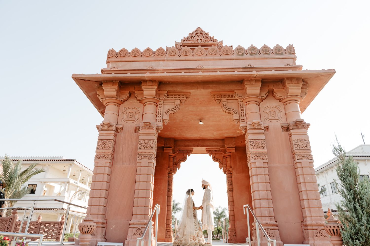 Ornate pink sandstone entrance gate with decorative carvings at a Hindu temple in traditional Indian architectural style.