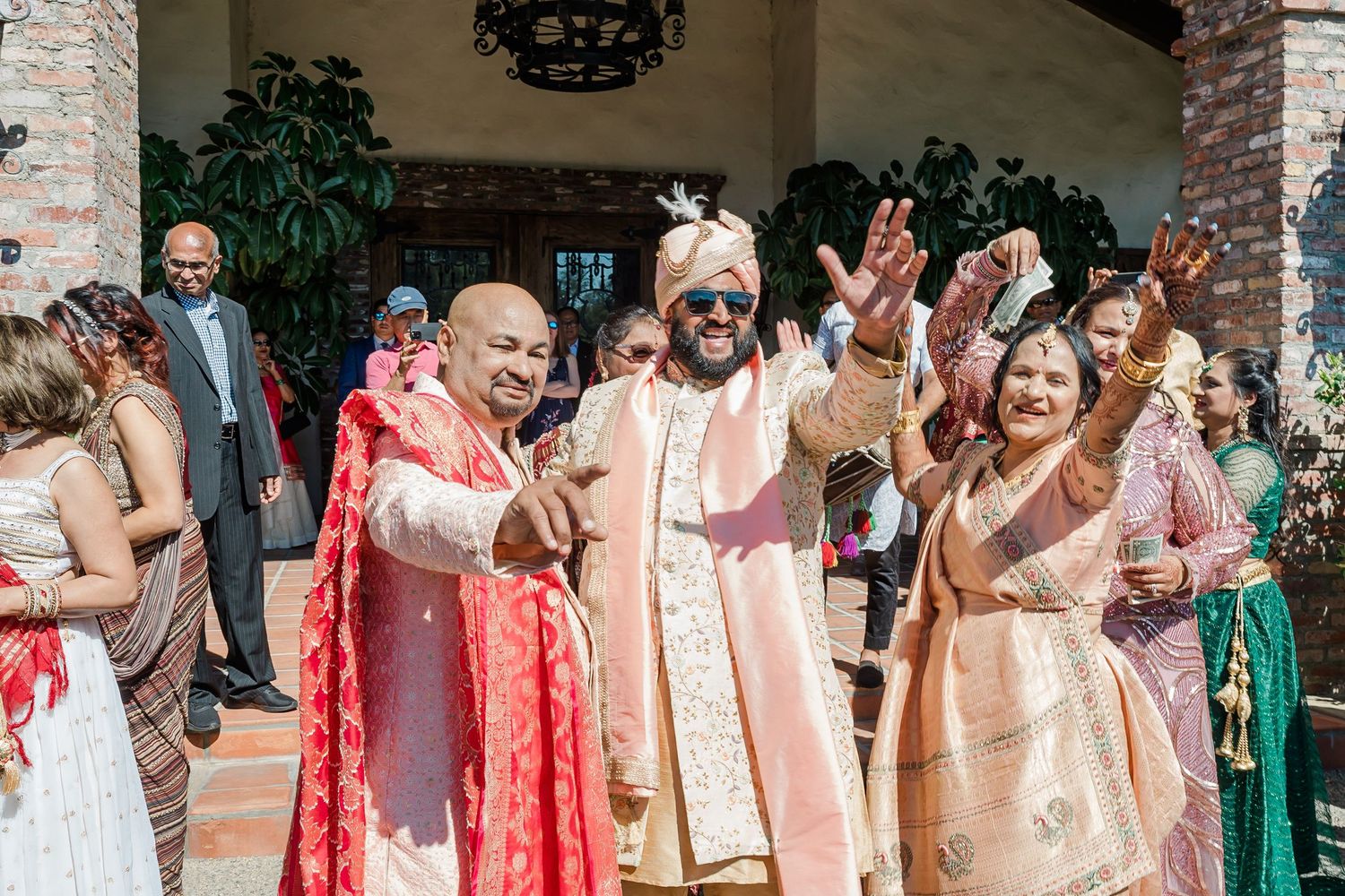 Wedding guests in traditional South Asian attire gather for celebration photos outdoors.
