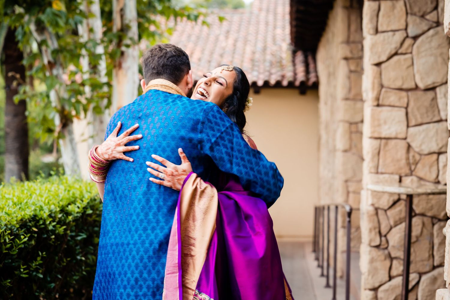 A couple embraces in a romantic moment on a stone patio surrounded by lush greenery.