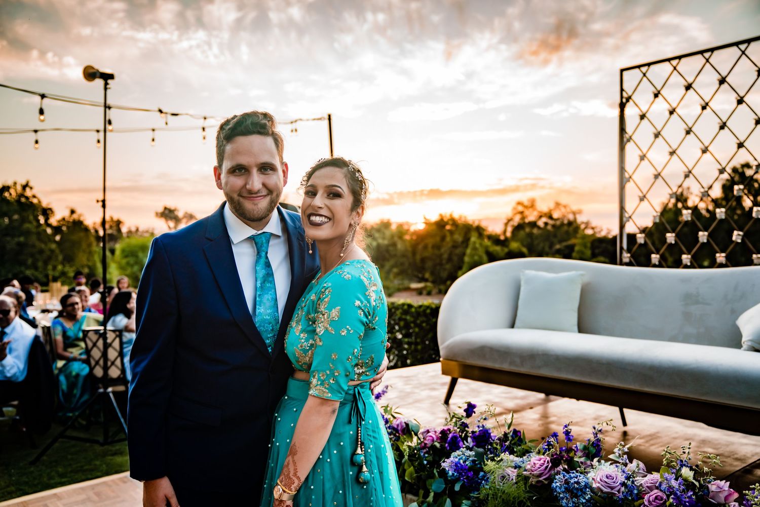 Sunset wedding celebration with guests enjoying cocktail hour on an outdoor patio decorated with string lights.
