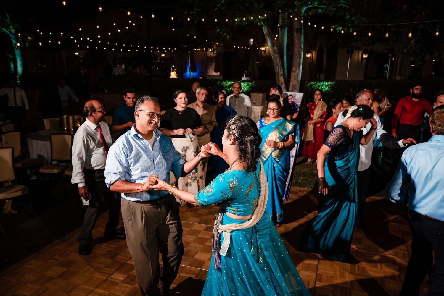 Wedding guests dance and celebrate on a dimly lit dance floor at an evening reception.