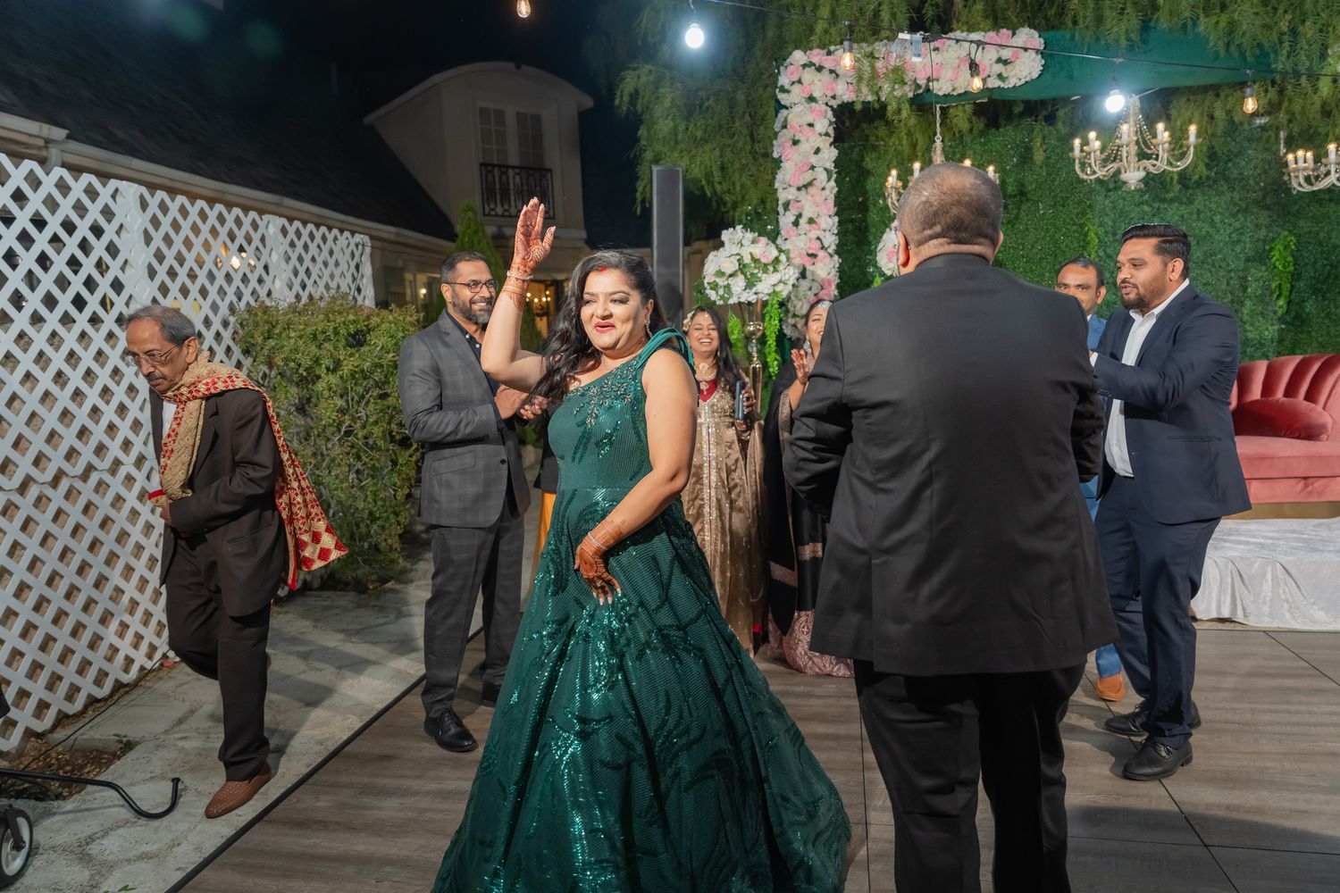 Elegant outdoor wedding reception with guests mingling under string lights and white lattice decor.