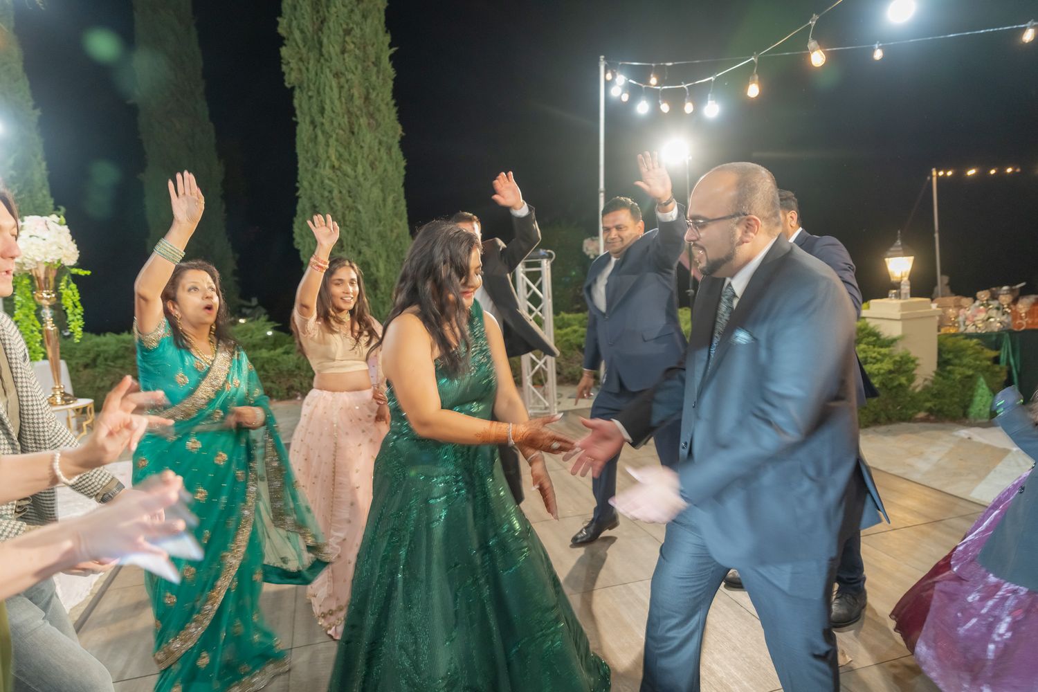 Evening wedding celebration showing guests dancing and socializing under twinkling outdoor lights.