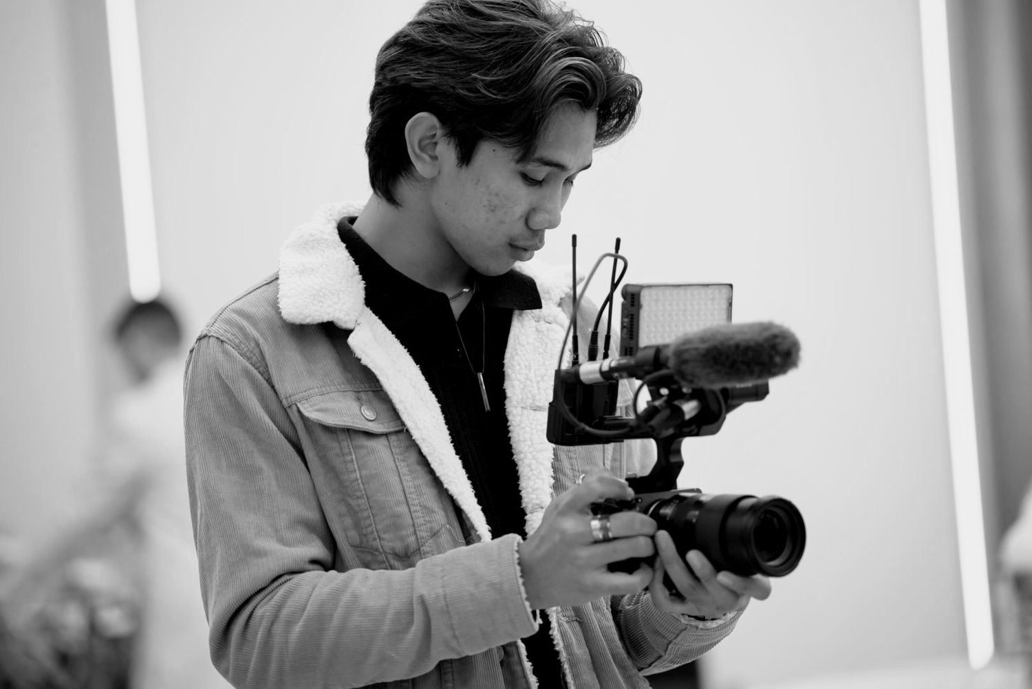 Young man holding a professional camera rig in black and white photography studio setting.