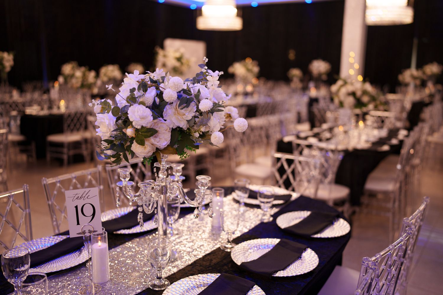 Elegant wedding reception tables decorated with crystal chandeliers, purple accents, and white floral centerpieces.