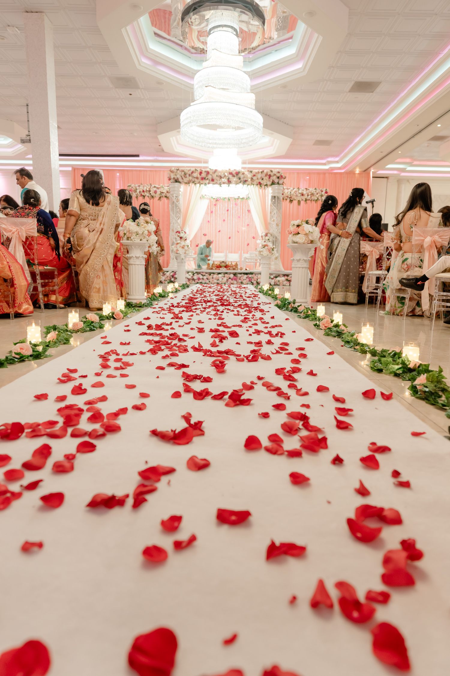 Elegant white wedding venue aisle scattered with red rose petals and lined with floral arrangements.