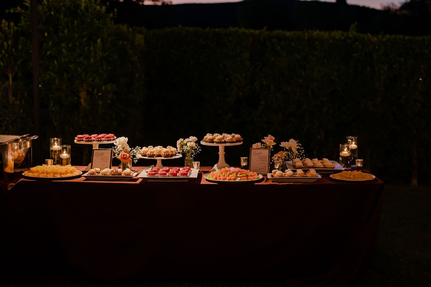 Rustic wooden dessert table display with multiple tiers of treats and sweets at a wedding reception.