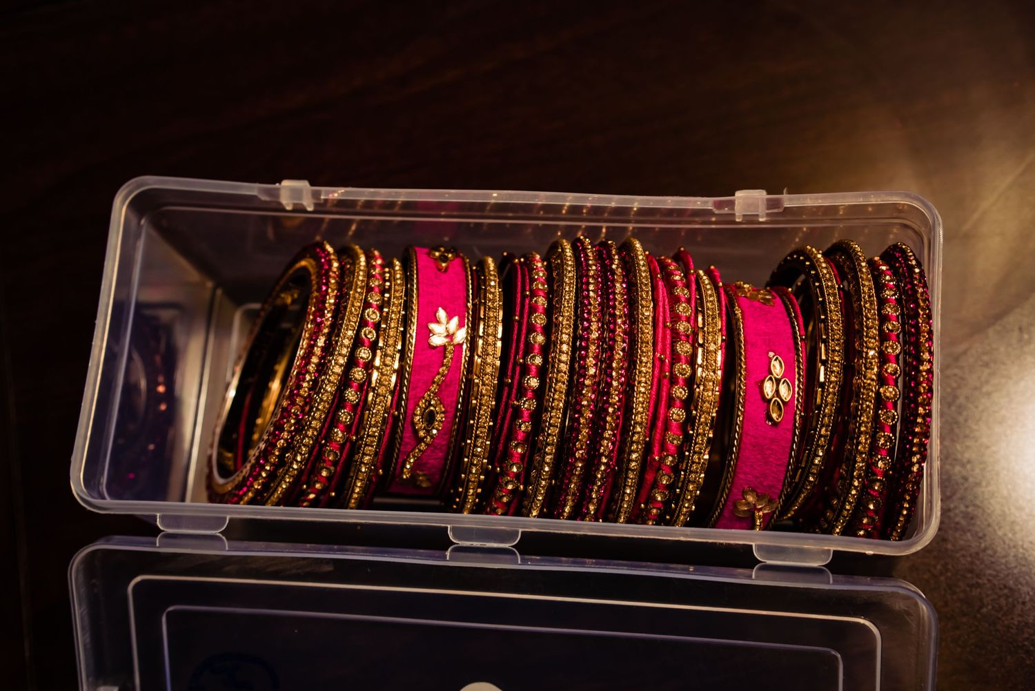 A collection of traditional Indian bangles with gold and red designs displayed in clear storage containers.