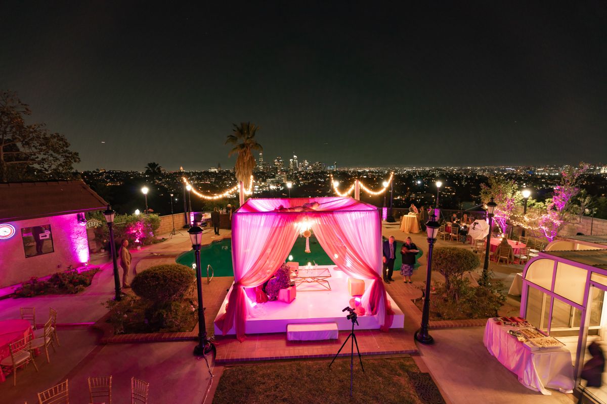 Outdoor wedding venue at night illuminated with pink and purple lighting and draped fabric decorations along the beach.