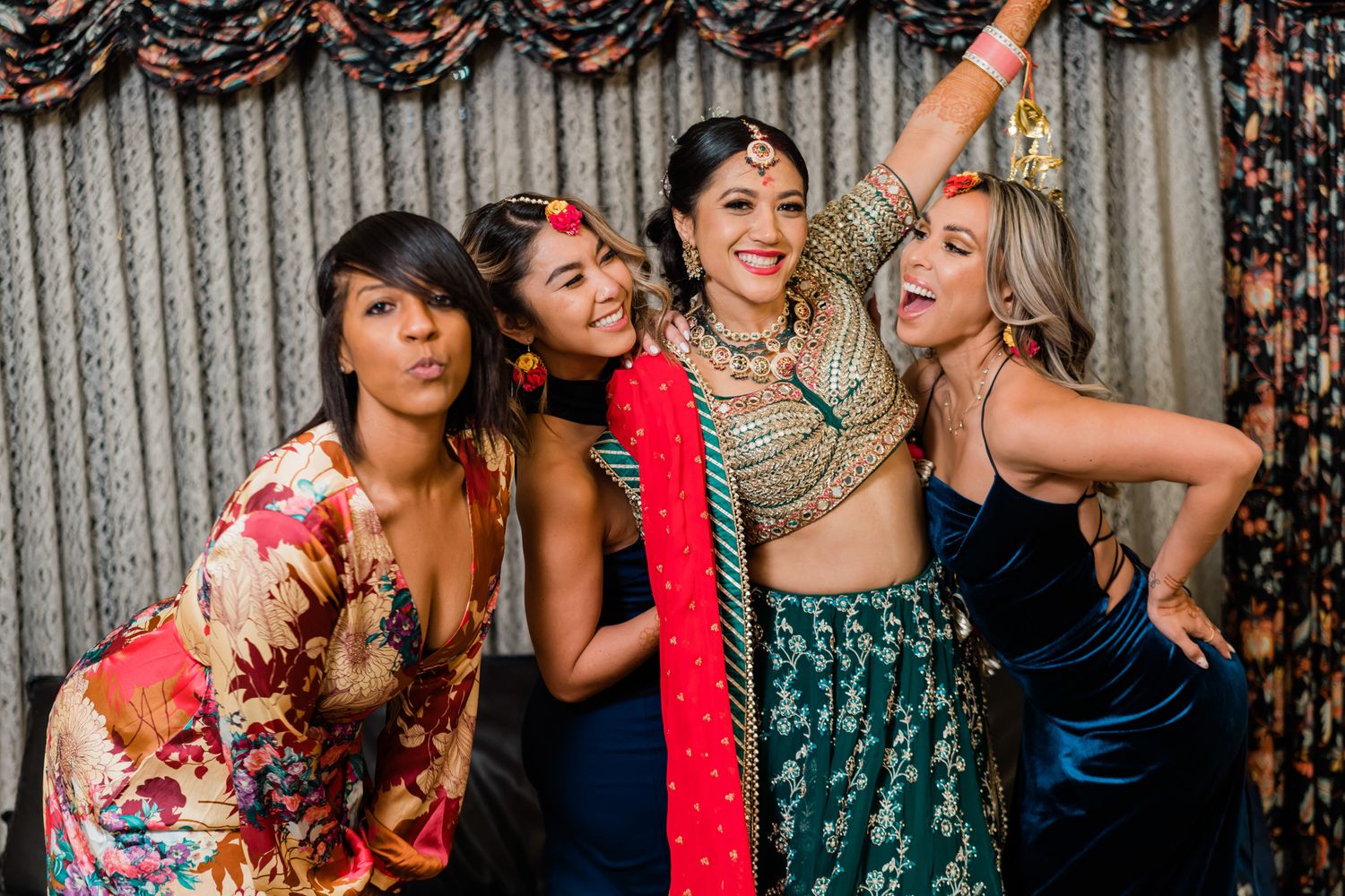 Women in formal attire share joyful moments at a festive gathering with decorative backdrop.