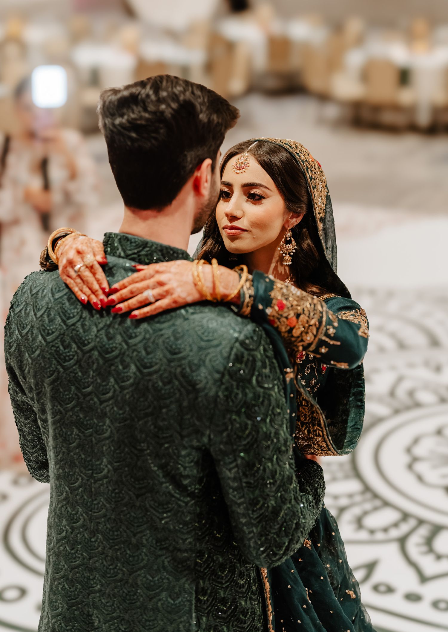 Couple embracing in traditional South Asian wedding attire on decorated dance floor.