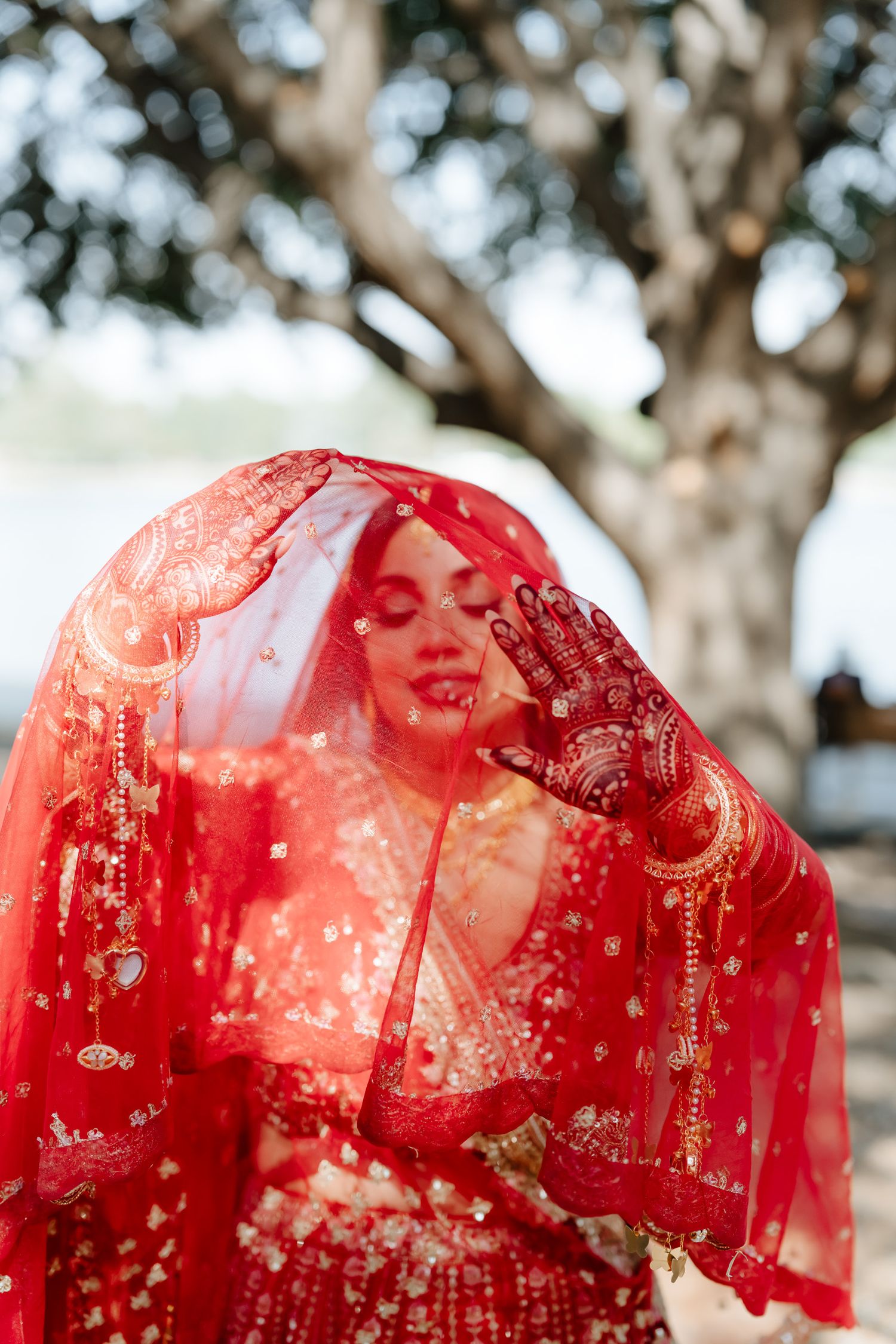 Ethereal portrait through a red veil showing intricate bridal jewelry and henna details.