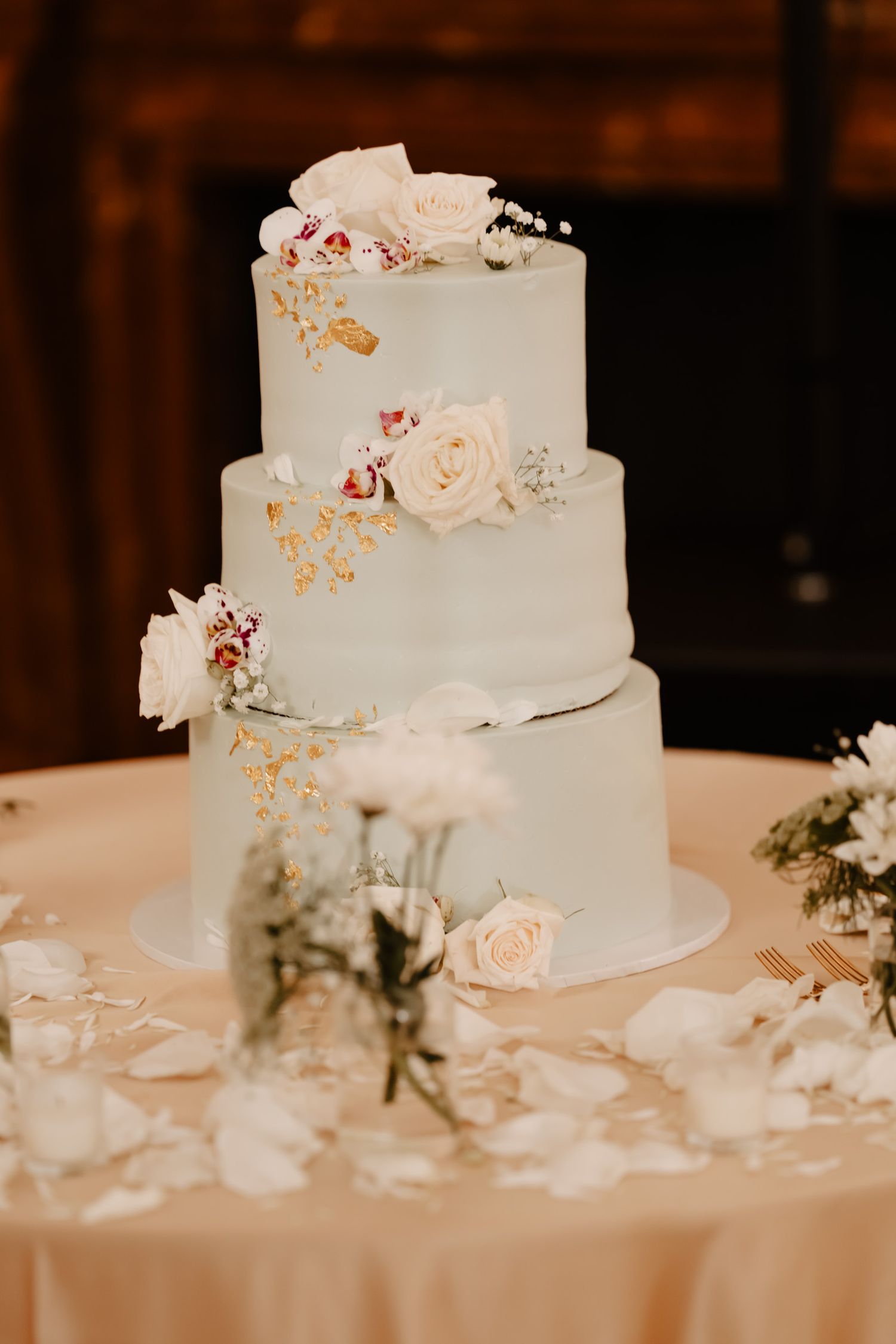 An elegant white wedding cake decorated with delicate roses and gold accents sits on a white tablecloth.