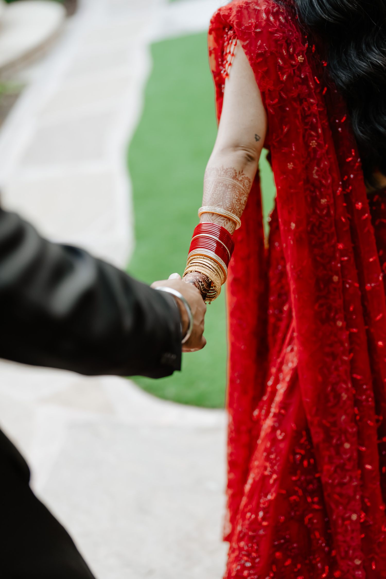 Close-up of traditional gold bangles and henna adorned hands holding against a red dress backdrop.