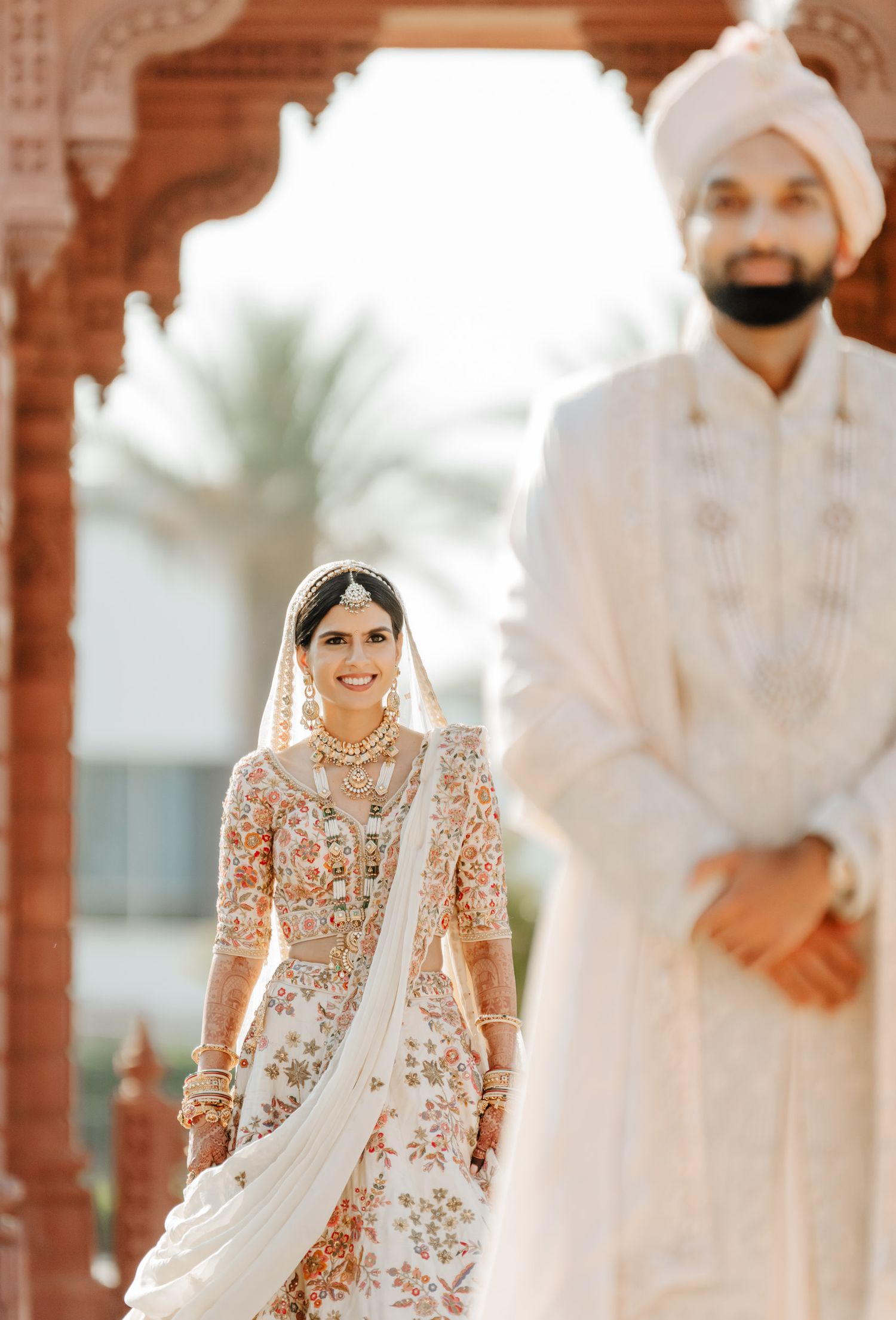 Traditional Indian wedding ceremony under ornate red sandstone architecture with palm trees.