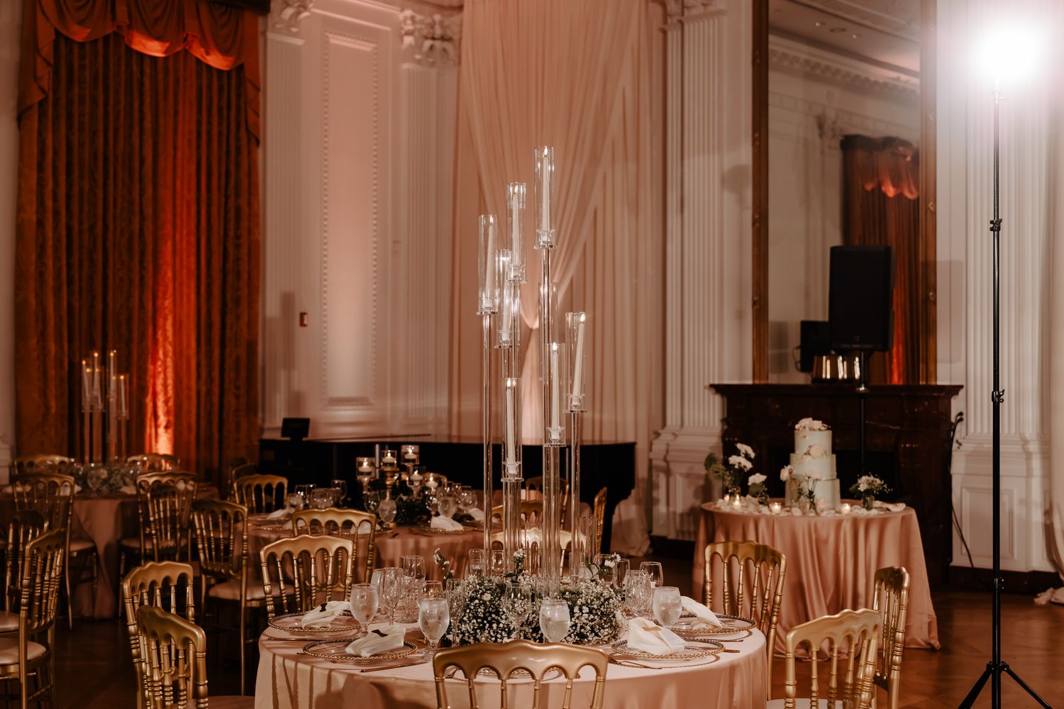 Elegant wedding reception table with tall crystal centerpieces and gold chiavari chairs in a grand ballroom.