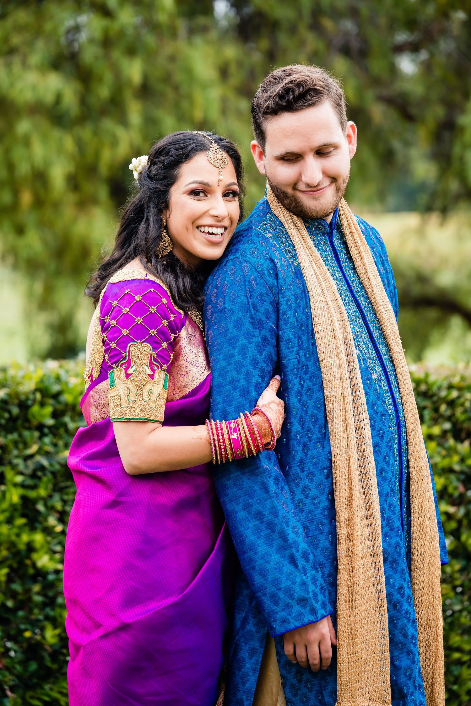 A couple in traditional Indian attire share joyful moments together in an outdoor garden setting.