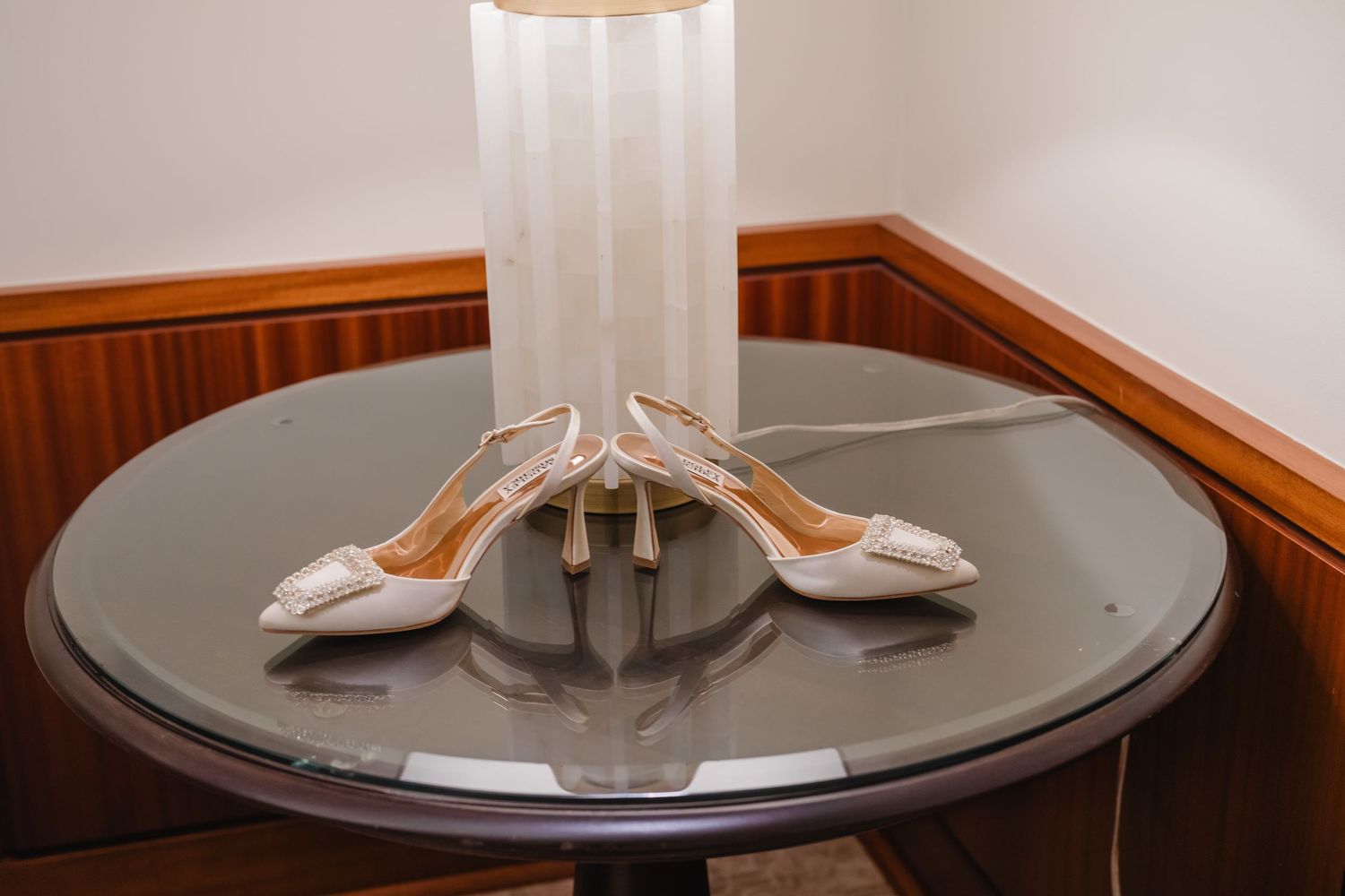 A white ceiling light fixture with multiple bulbs hangs from a wood-paneled ceiling above a round glass table.