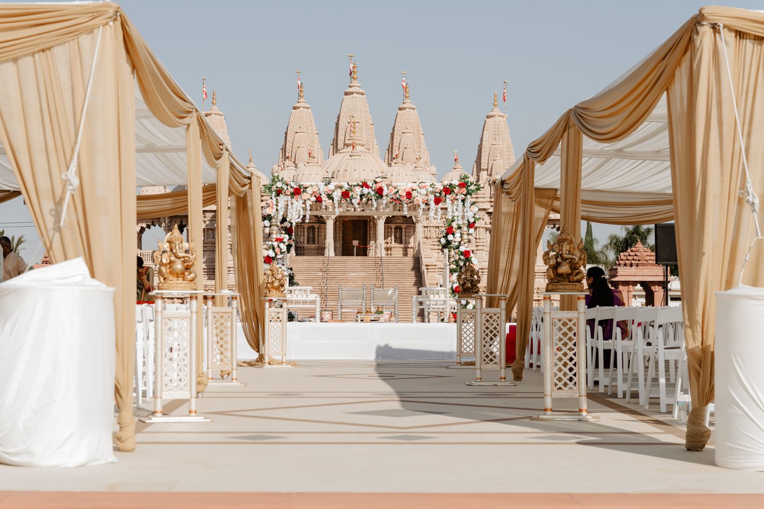 Elegant wedding mandap with flowing champagne fabric drapes and crystal chandeliers in an ornate venue.