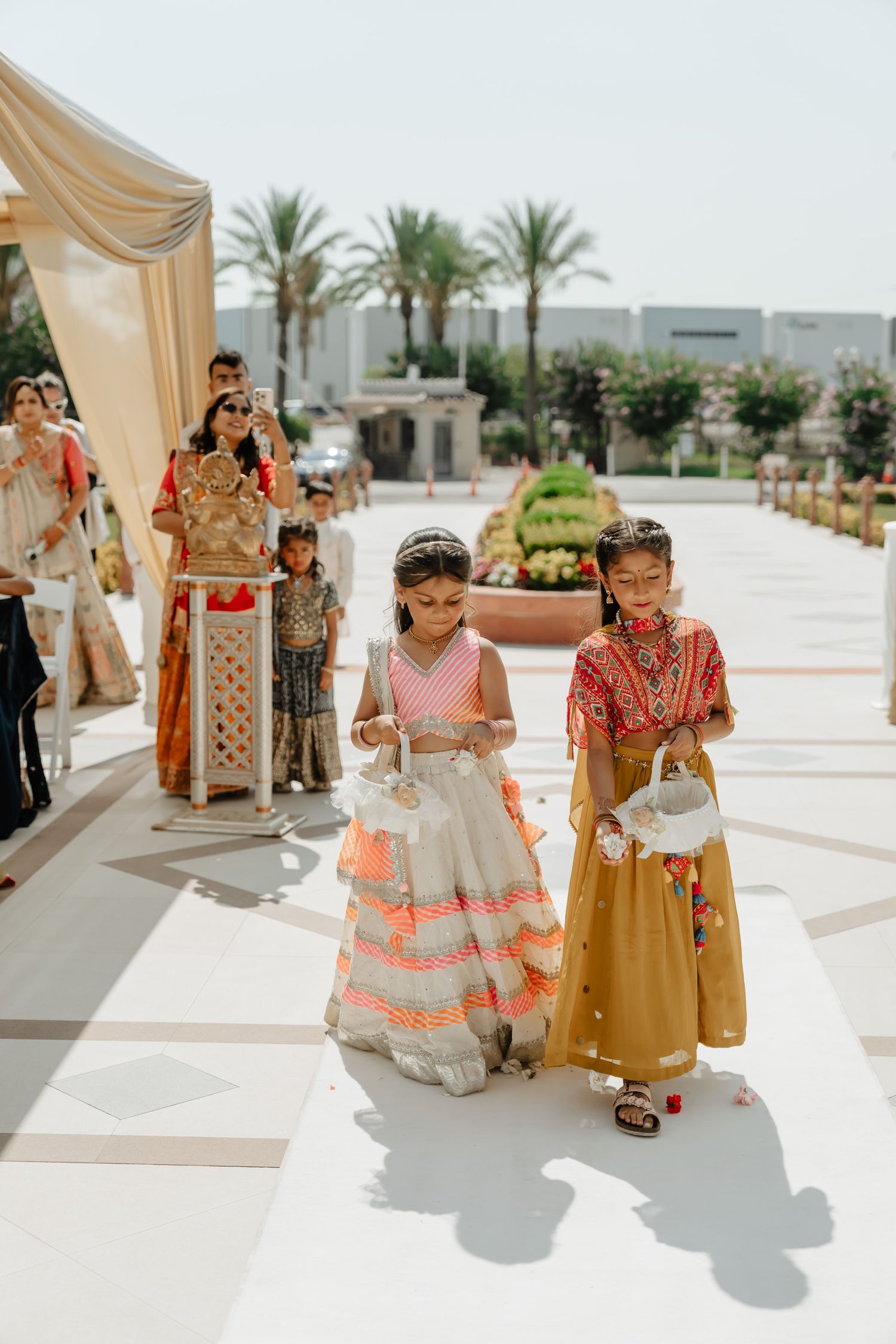 Children in colorful traditional Indian attire walking together at an outdoor wedding venue.