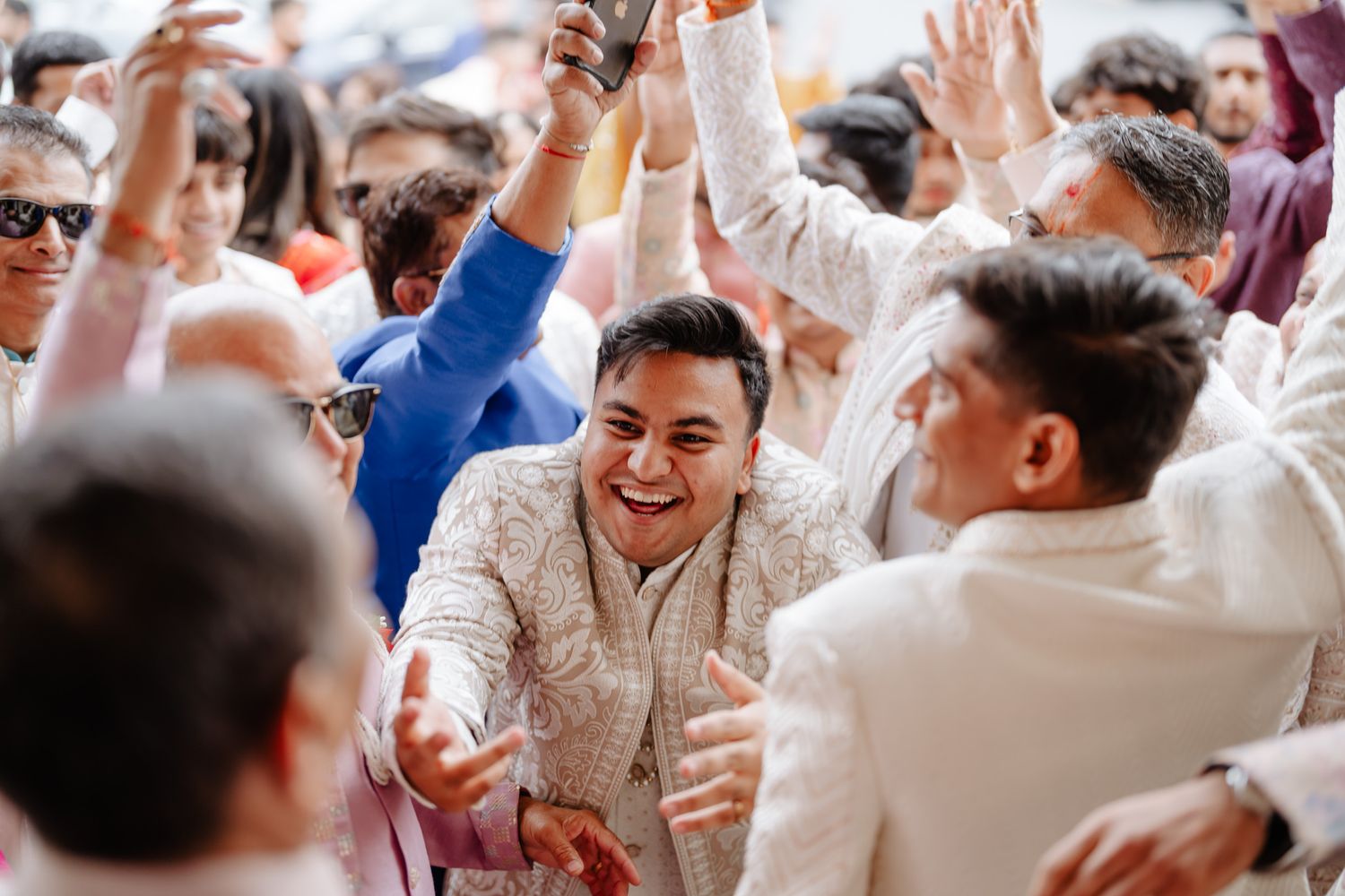 A group of wedding guests dancing and celebrating with raised hands at a lively reception party.