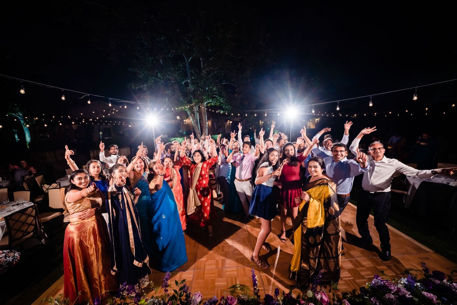 Silhouettes of people dancing and celebrating at a nighttime outdoor event with bright spotlights illuminating the scene.