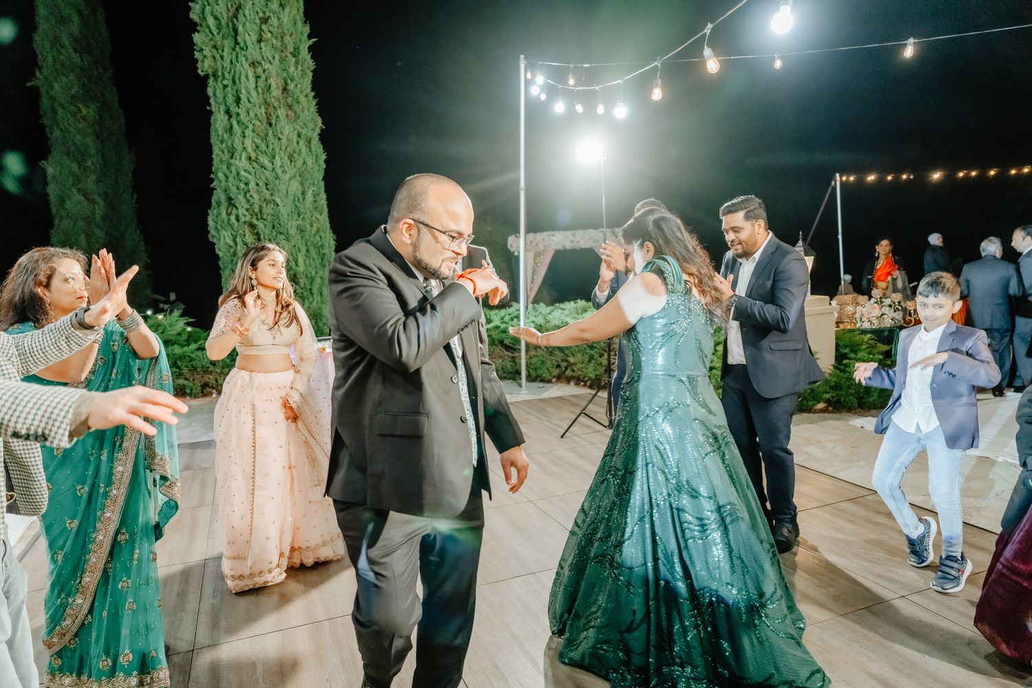 Guests dancing and celebrating under outdoor string lights during an evening event.