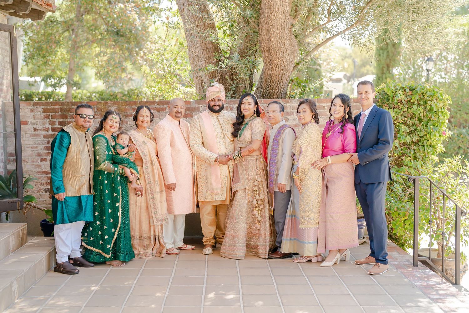 A group photo of wedding guests in traditional South Asian formal attire gathered outdoors for a celebration.