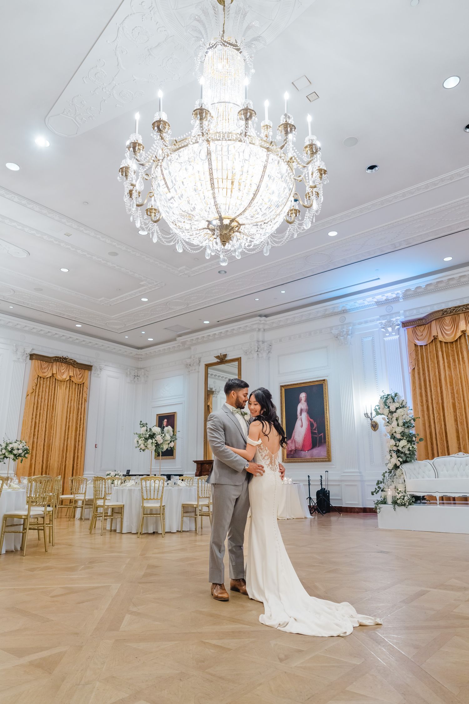 Elegant ballroom with crystal chandeliers and hardwood floors showcases couples dancing in formal attire.