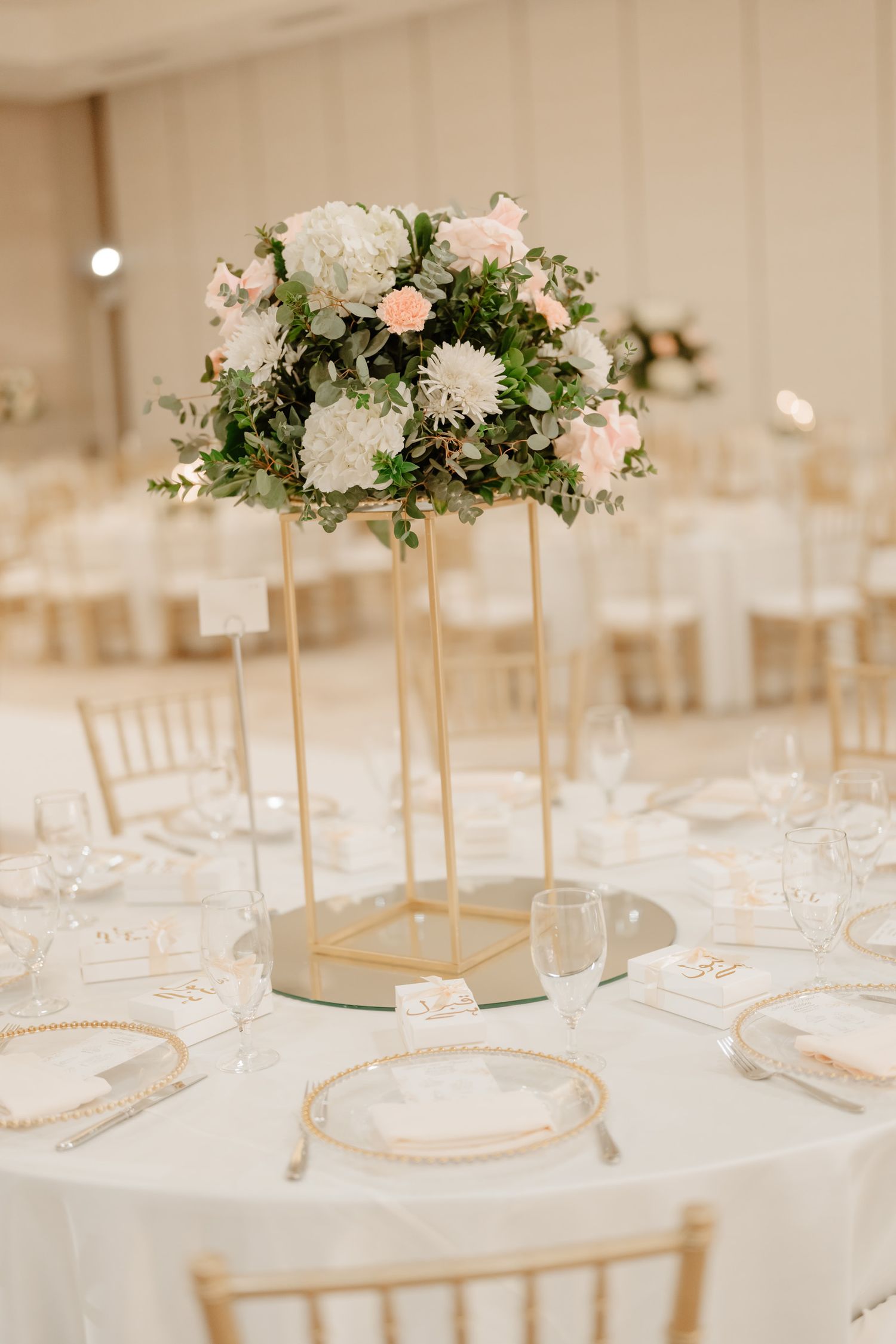 Elegant wedding centerpiece with white and pink flowers on gold stands atop white tablecloth setting.