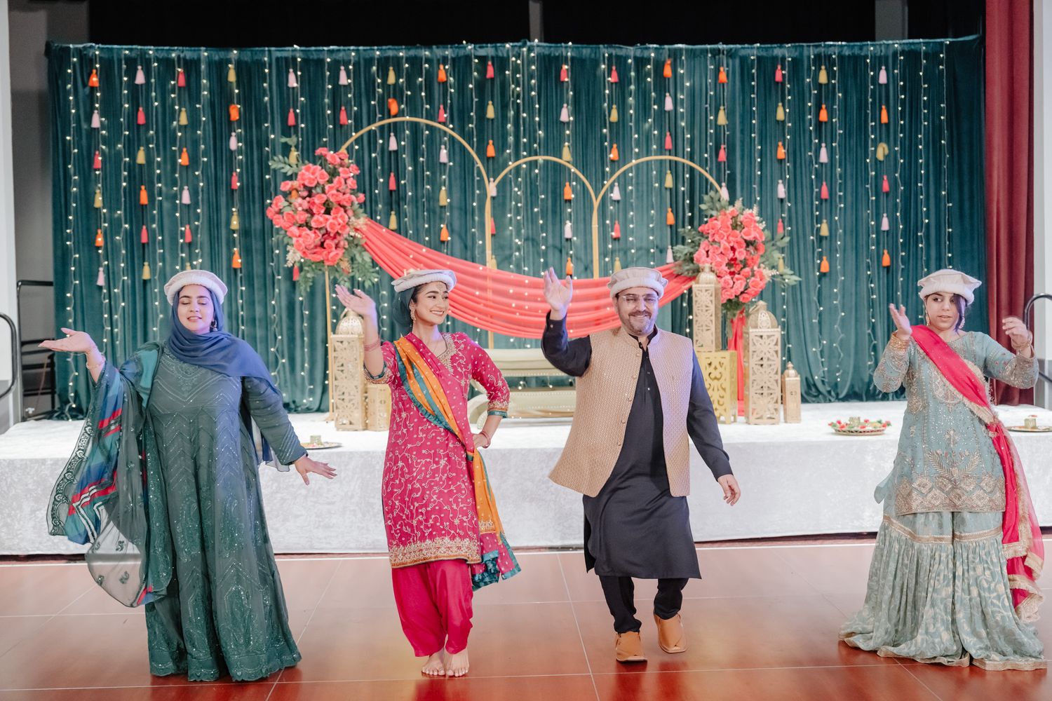 Traditional South Asian wedding celebration with dancers in colorful attire under teal decorative backdrop.