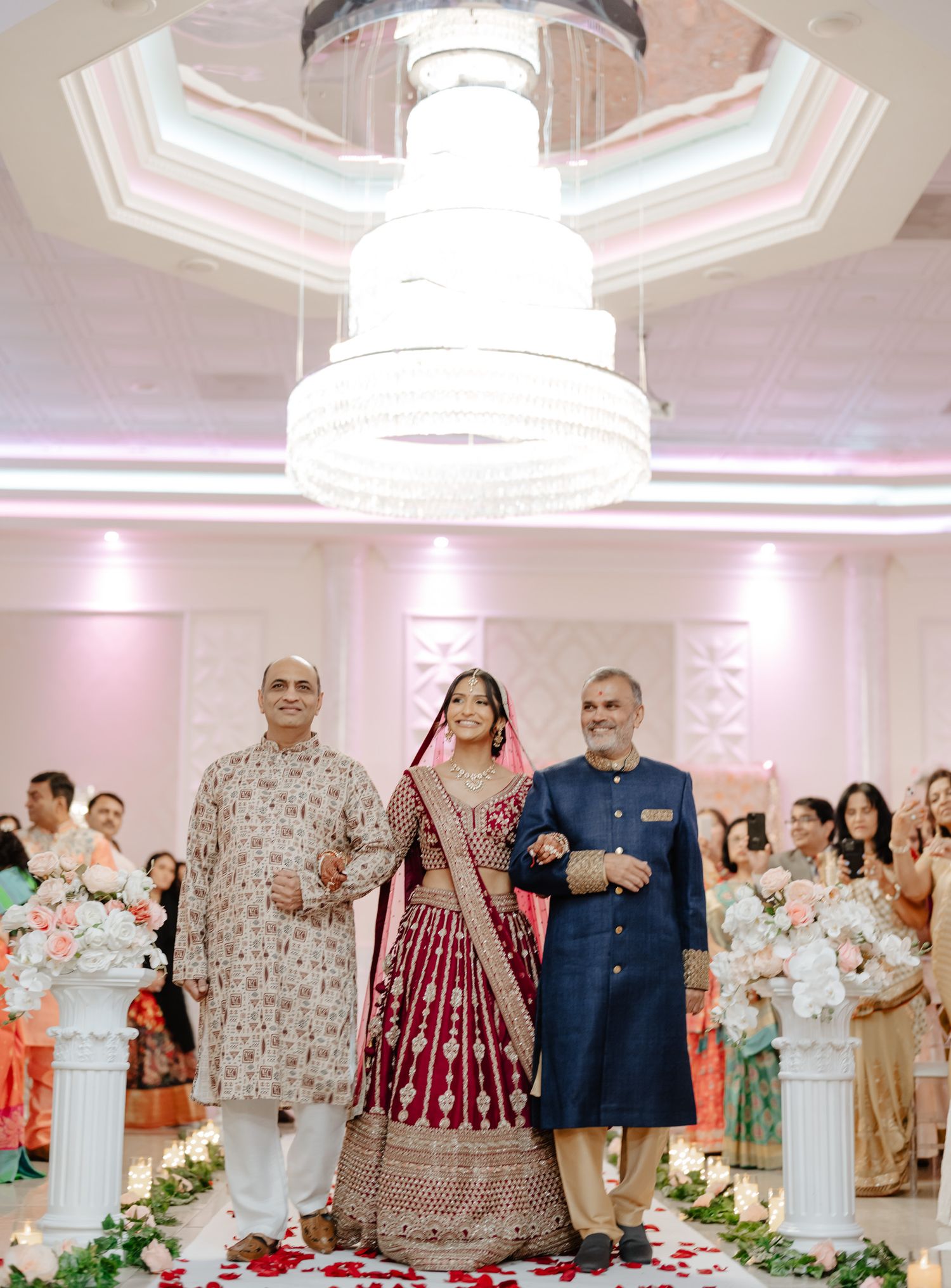 Traditional Indian wedding ceremony in an elegant ballroom with grand chandelier and floral decorations.