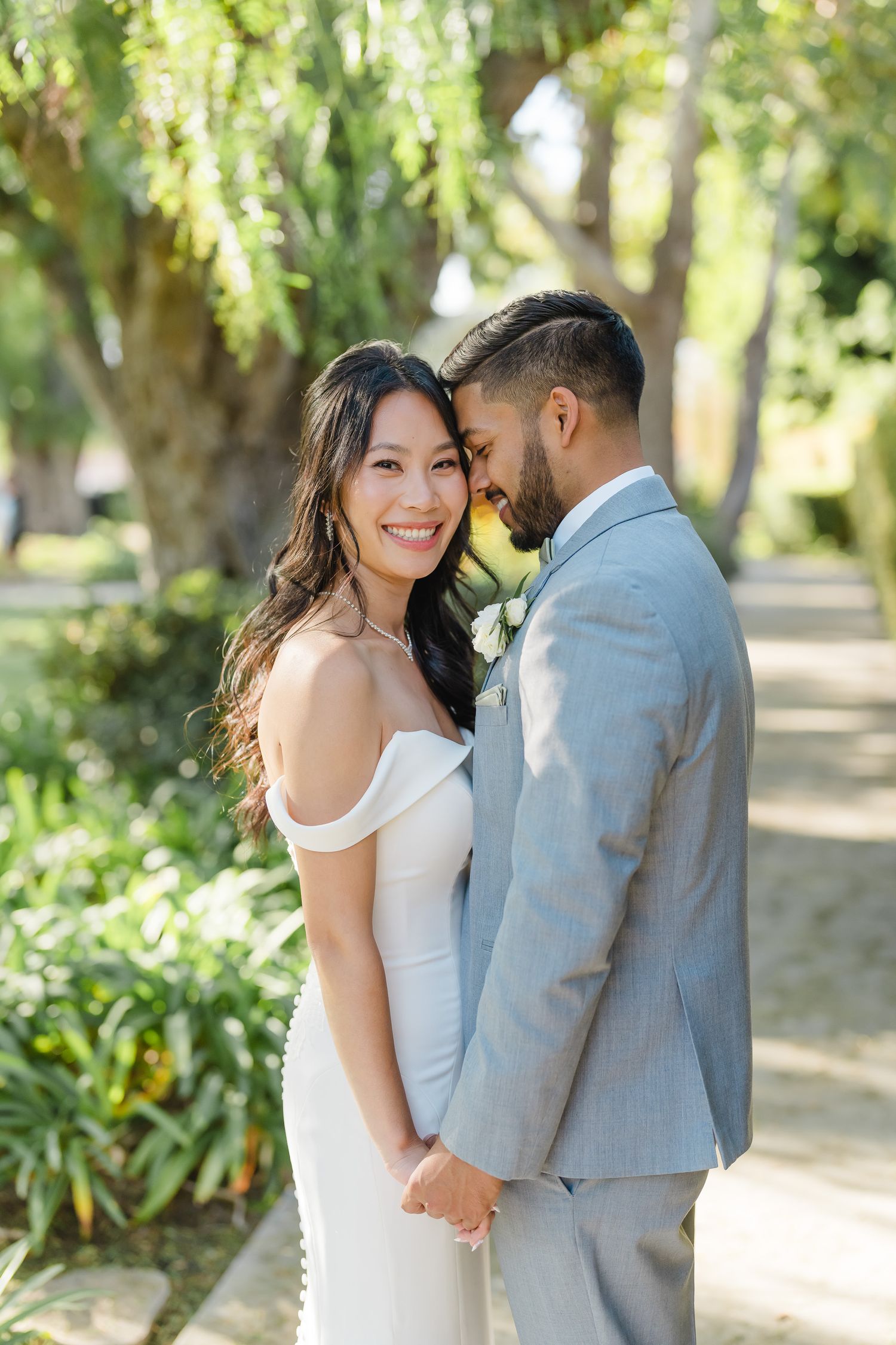 Newlywed couple sharing intimate moments in a sunlit garden pathway.