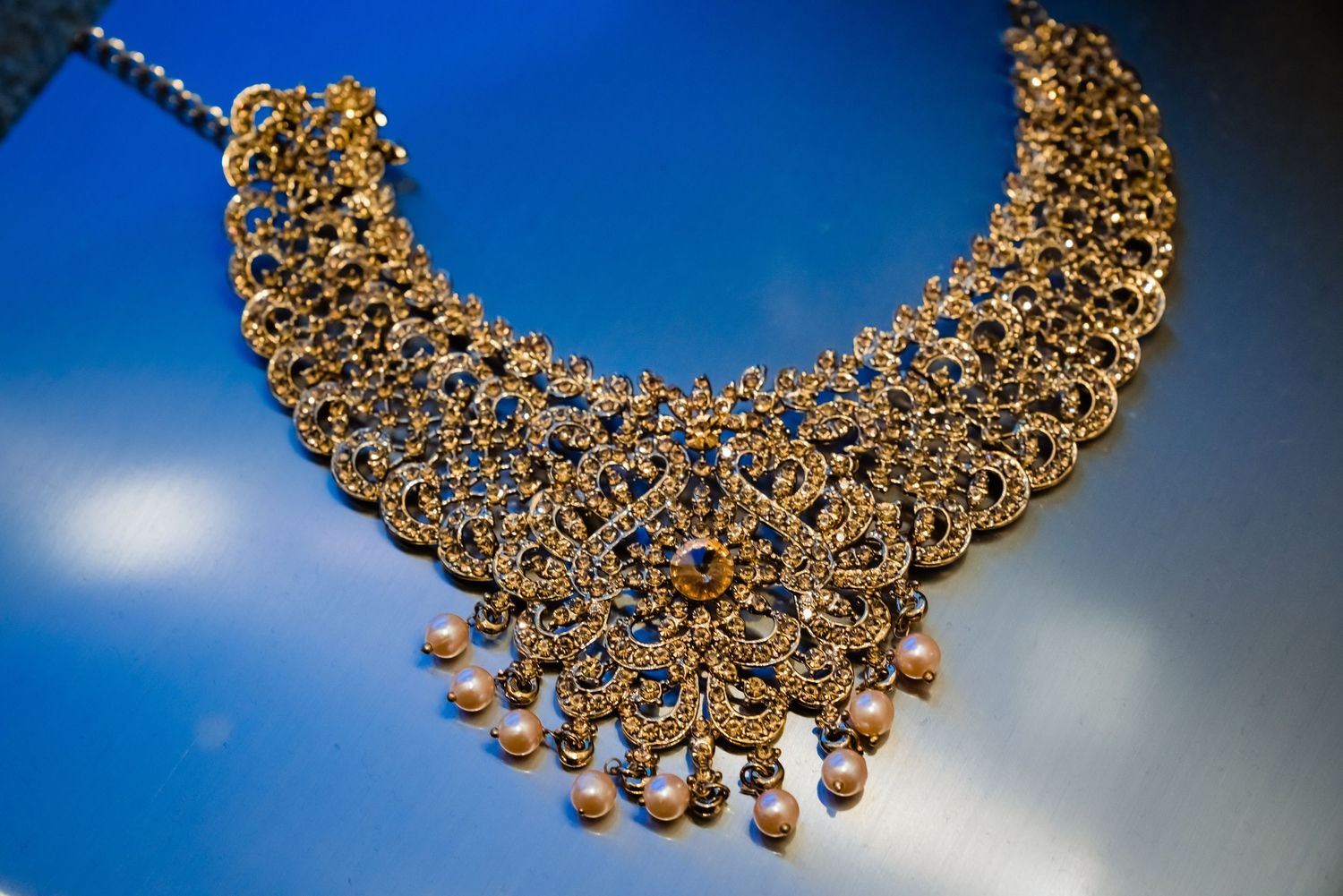A close-up sequence of a golden ornate necklace against a blue background shows different angles of its intricate design.