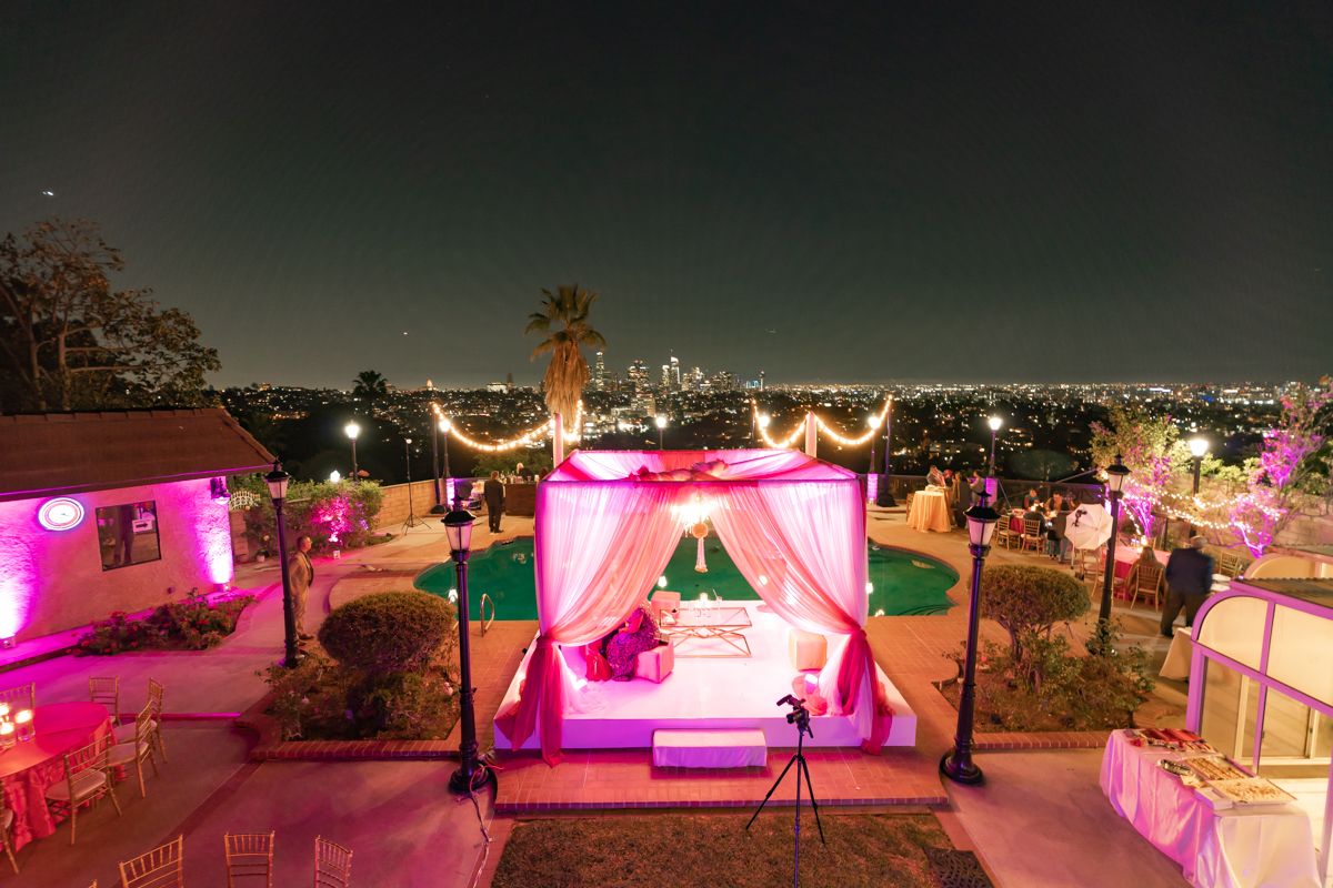 Panoramic view of an outdoor wedding venue illuminated with pink and purple lights at dusk.