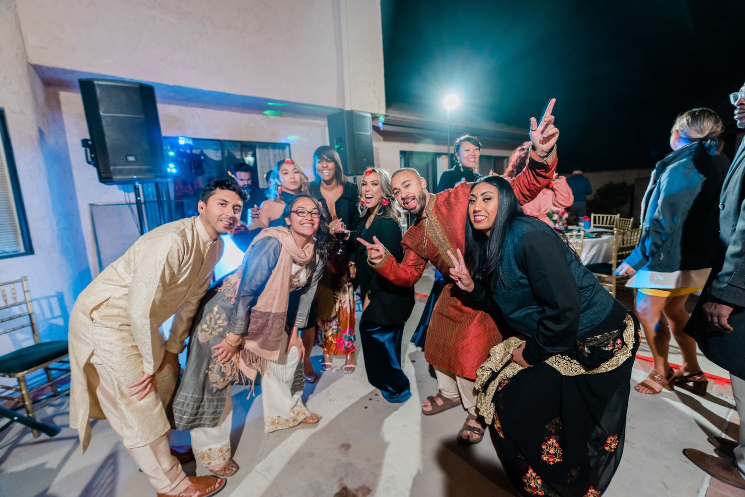 Large group of party guests dancing together on a dark dance floor with blue lighting.