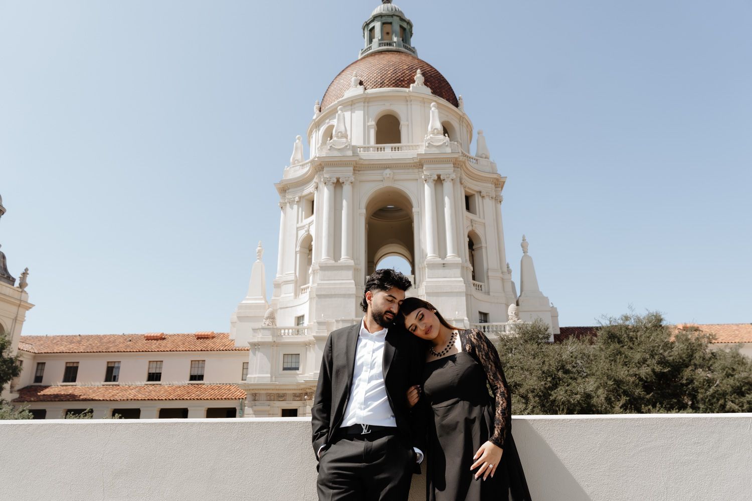 Elegant couple standing together before Pasadena City Hall, man in suit and woman in black jacket.