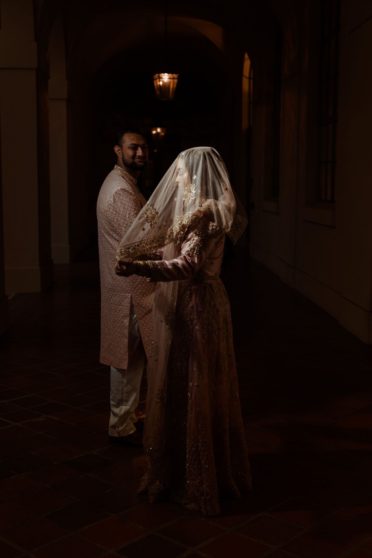 A moody evening portrait of a couple in traditional wedding attire under dim lighting.